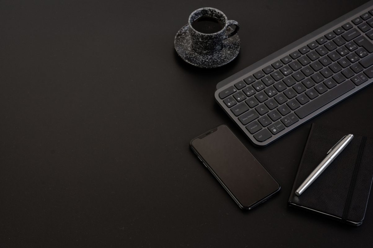 Dark desk with phone, keyboard and notebook set up for remote collaboration